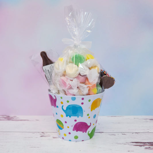 Our Baby Basket is a perfect gift for baby showers, new parents, or proud grandparents. Each baby-themed container is filled with a delightful mix of candy favorites including:
8 ounces of soft, chewy salt water taffy in an assortment of classic flavors, milk chocolate nonpareils, and a handmade milk chocolate baby bottle lollipop, all wrapped up and ready to gift.
