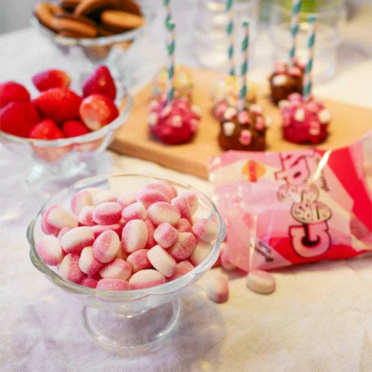 Candy bar with pink and white candies, red fruits, and cake pops on a table.
