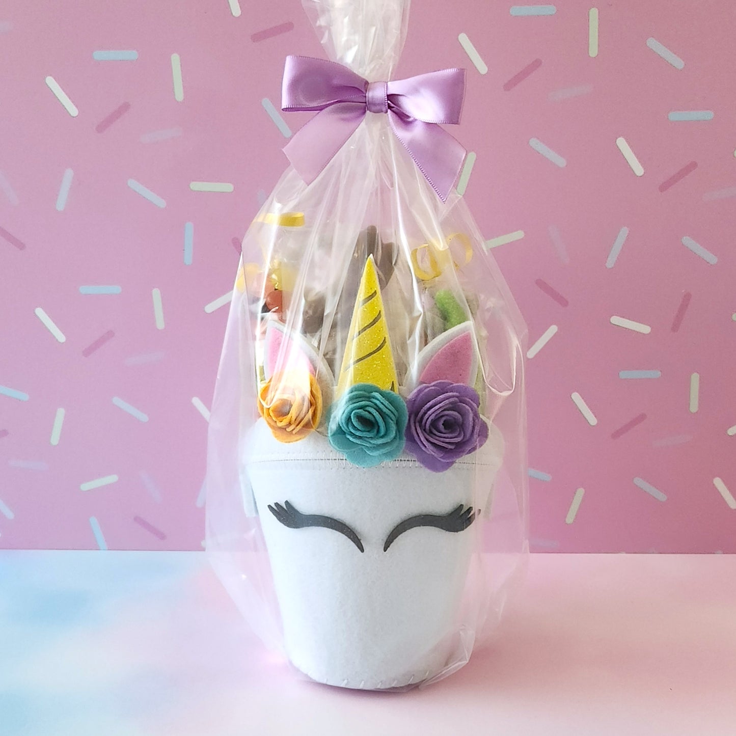 Felt Unicorn basket. Contains Chocolate Dipped Marshmallow Peeps, Jelly Beans, Sanded Gummi Bunnies and a Chocolate Bunny Favor. We finish the basket with overwrap and a bow so that it is ready to gift!