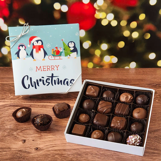 Box of chocolates with a Christmas card on a wooden surface with a festive background.