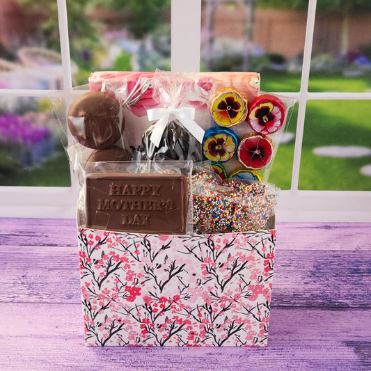 Mother's Day Pink Blossom Gift Basket. This beautiful basket is filled with a 16-piece assortment of our most-loved chocolates—smooth meltaways, gooey caramels, creamy soft centers, and rich truffles. We didn’t stop there! We also added milk chocolate foiled flowers, chocolate-covered Oreos, classic milk chocolate nonpareils, and some dark chocolate-covered cranberries for a little fruity twist. The star of the show? A milk chocolate card that says “Happy Mother’s Day”