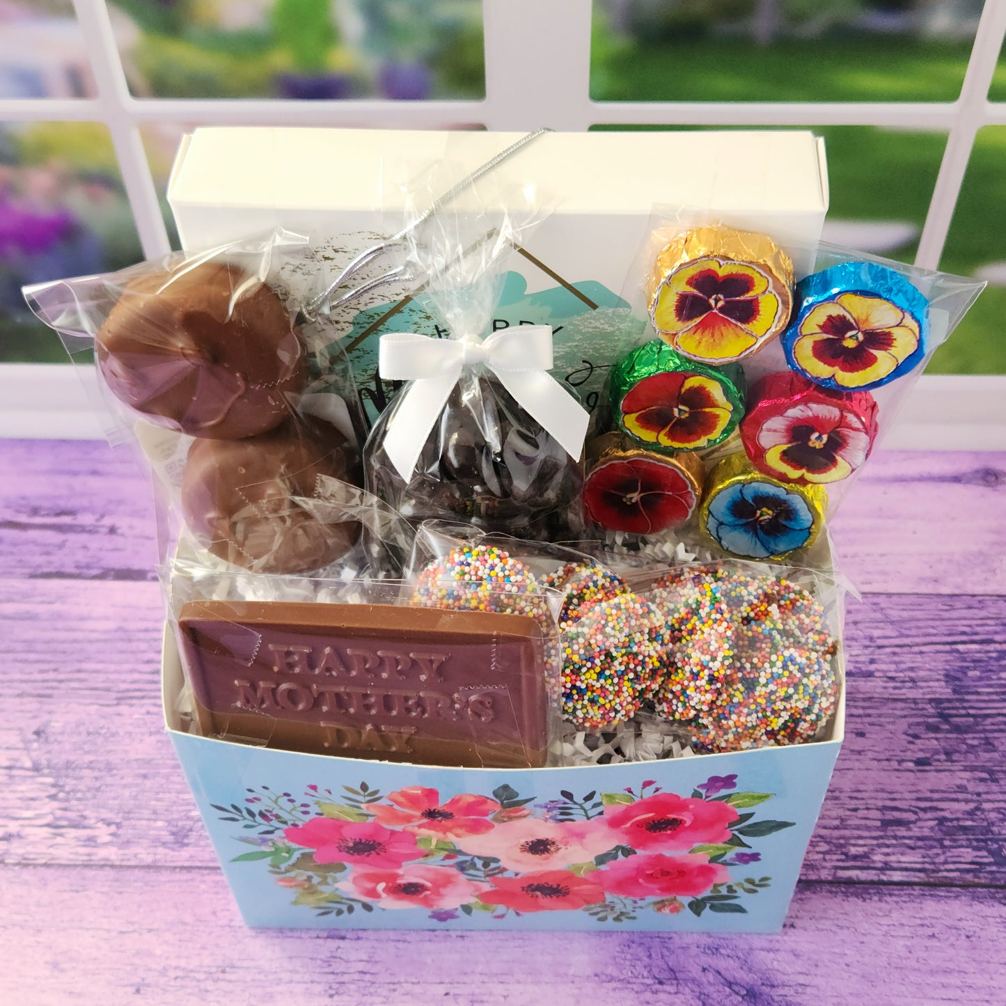 Mother's Day Watercolor Flower Gift Basket. This beautiful basket is filled with a 16-piece assortment of our most-loved chocolates—smooth meltaways, gooey caramels, creamy soft centers, and rich truffles. We didn’t stop there! We also added milk chocolate foiled flowers, chocolate-covered Oreos, classic milk chocolate nonpareils, and some dark chocolate-covered cranberries for a little fruity twist. The star of the show? A milk chocolate card that says “Happy Mother’s Day”