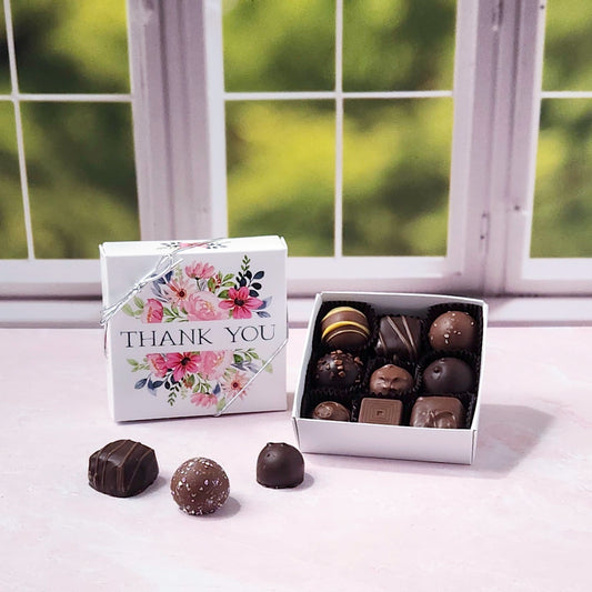 Box of chocolates with a 'Thank You' box on a windowsill with a blurred green garden background.