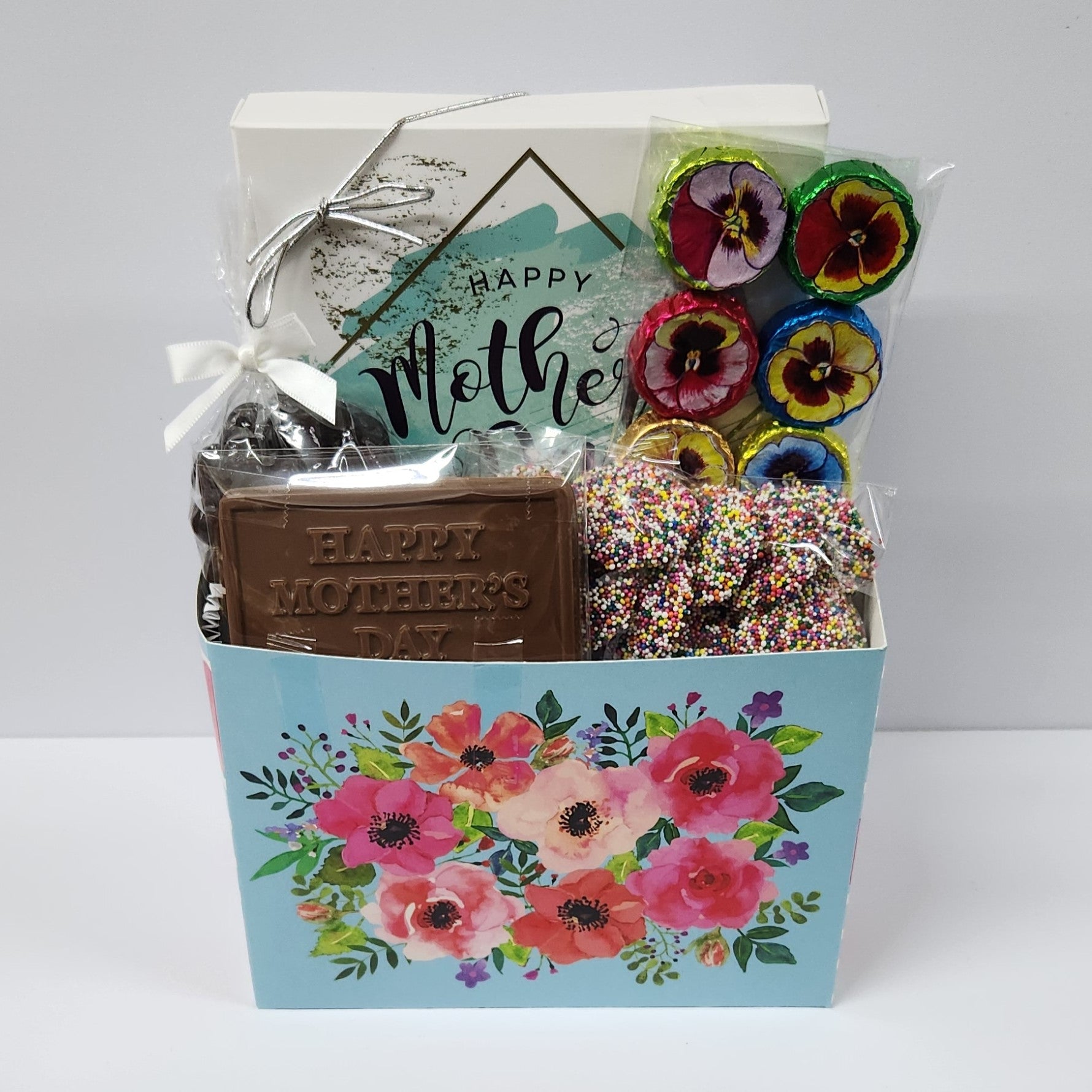 Watercolor Flowers Mother's Day Gift Basket featuring 16 piece assortment with creams, caramels, meltaways and truffles, milk chocolate foiled flowers, milk chocolate nonpareils, dark chocolate covered cranberries, and a chocolate card with the saying "Happy Mother's Day"