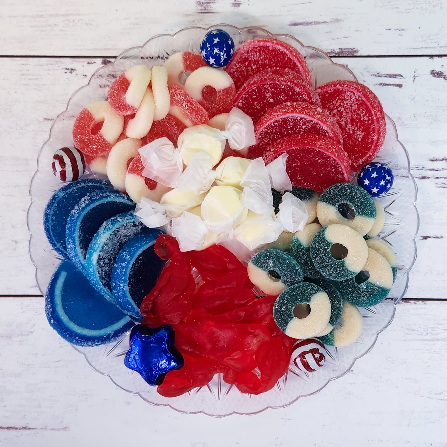 Brighten your summer festivities with our Summer Fun Party Dessert Platter, including patriotic Milk Chocolate Foiled Stars and Stripes, vibrant fruit slices, classic salt water taffy, fun gummi lobsters, refreshing watermelon rings, and zesty blue raspberry rings. Overwrapped and adorned with a festive bow, this delightful assortment is perfect for gift-giving or adding a splash of color and flavor to any summer celebration.