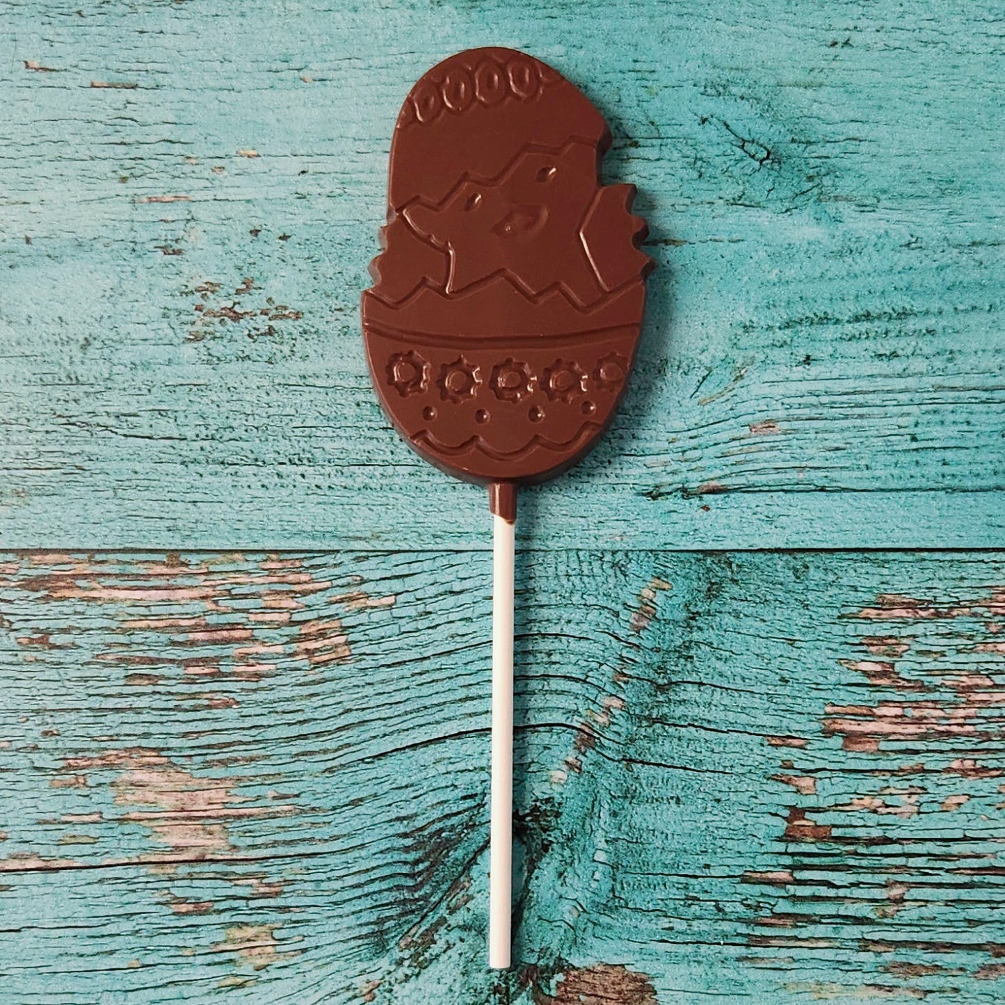 Chocolate lollipop shaped like a chick in an Easter egg on a wooden surface