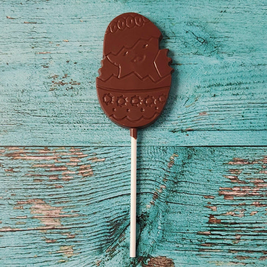 Chocolate lollipop shaped like a chick in an Easter egg on a wooden surface