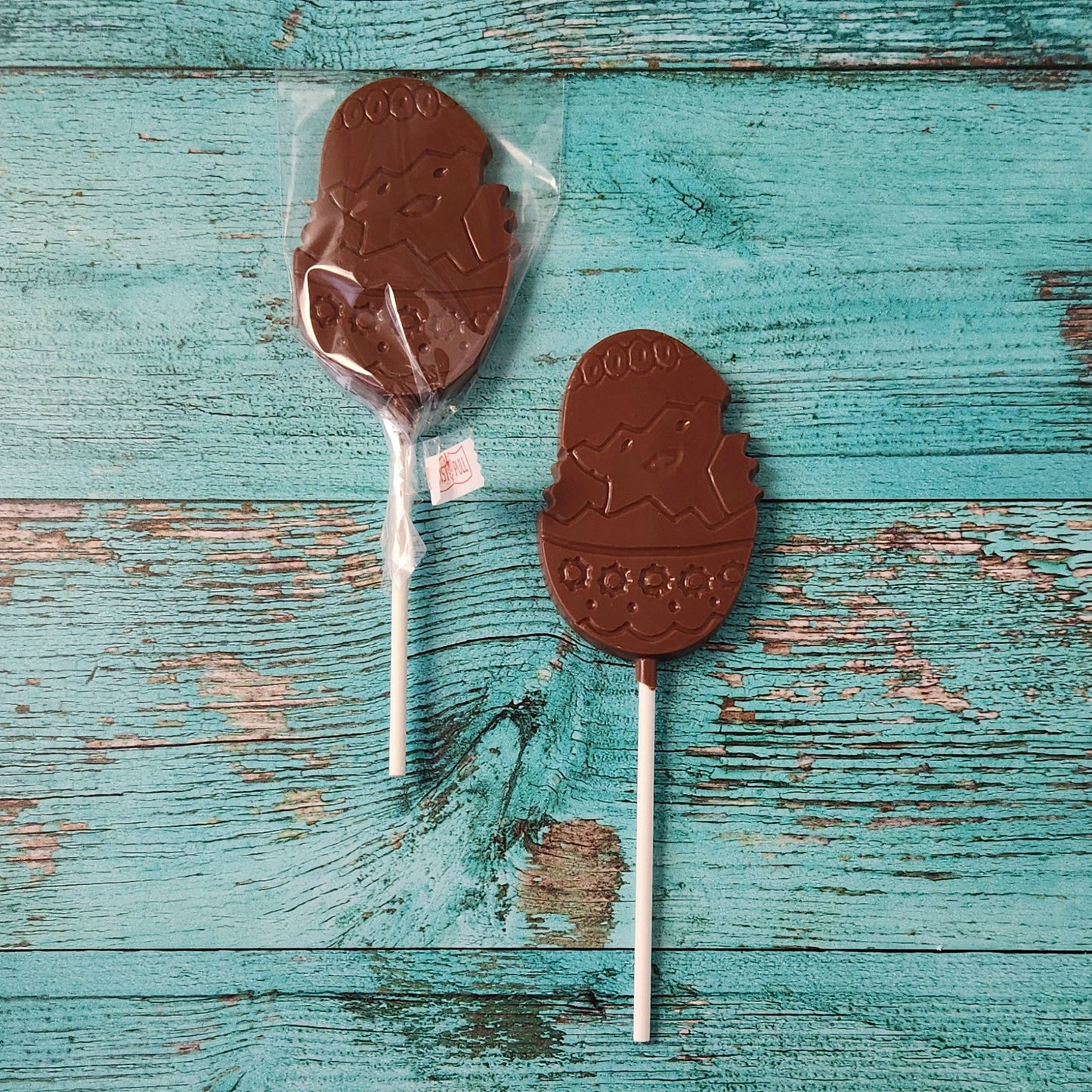 Two chocolate lollipops on sticks with a visible tag against a rustic wooden background.