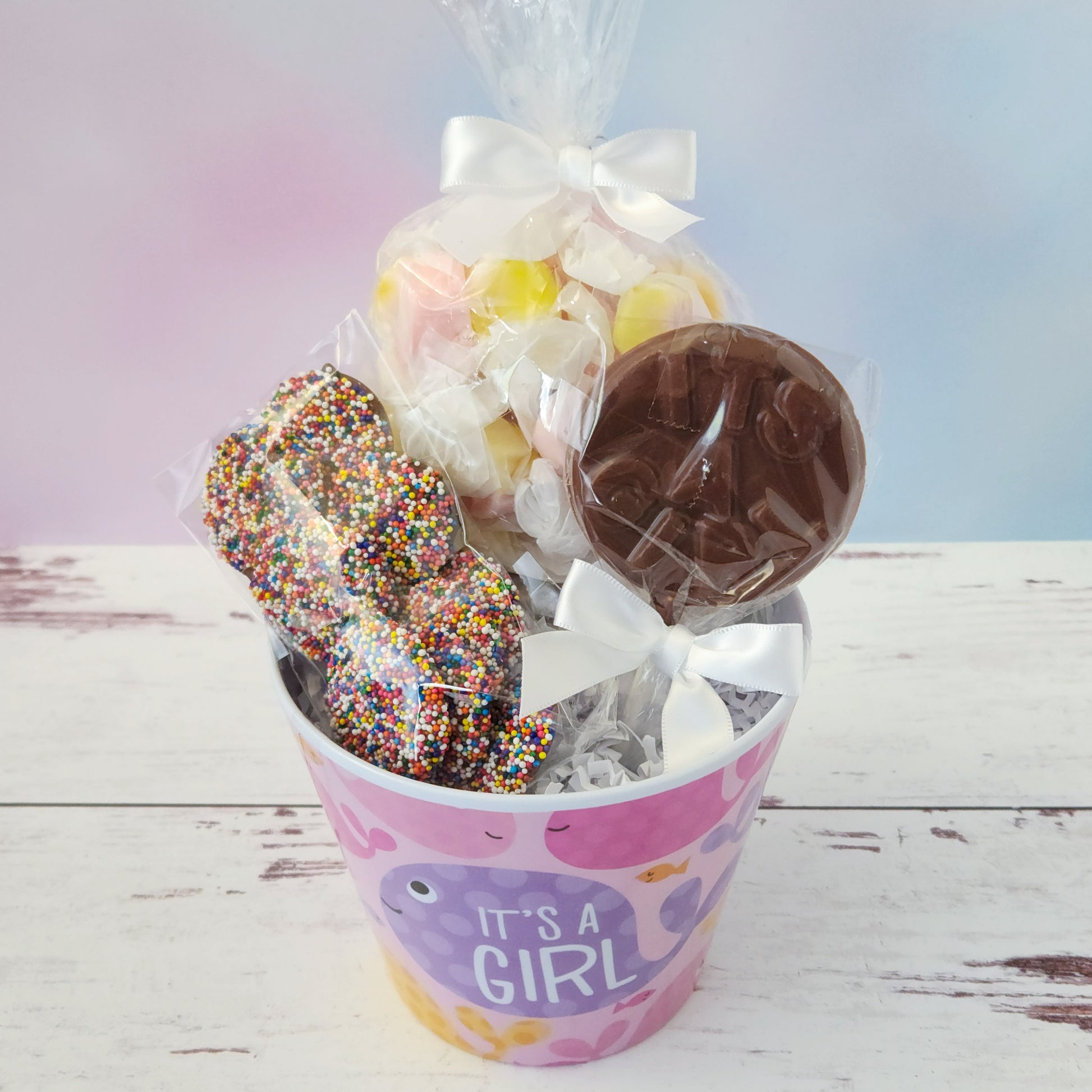 Our "It's a Girl" Baby Basket is a perfect gift for baby showers, new parents, or proud grandparents. Each baby-themed container is filled with a delightful mix of candy favorites including:
8 ounces of soft, chewy salt water taffy in an assortment of classic flavors, milk chocolate nonpareils, and a handmade milk chocolate "It's a Girl" lollipop, all wrapped up and ready to gift.