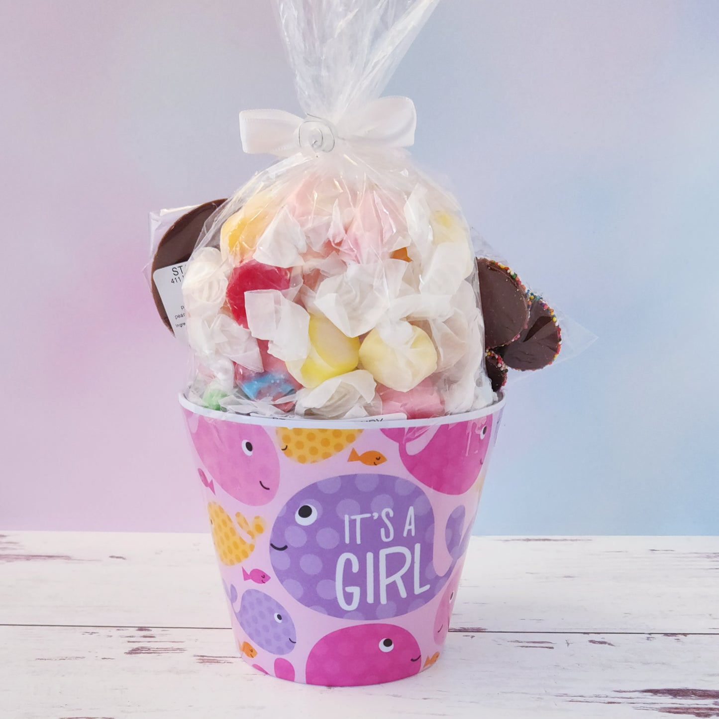 Our "It's a Girl" Baby Basket is a perfect gift for baby showers, new parents, or proud grandparents. Each baby-themed container is filled with a delightful mix of candy favorites including:
8 ounces of soft, chewy salt water taffy in an assortment of classic flavors, milk chocolate nonpareils, and a handmade milk chocolate "It's a Girl" lollipop, all wrapped up and ready to gift.