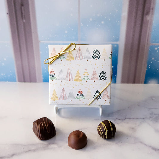 An assortment of our most popular milk and dark chocolate creams, caramels, melt-aways, and truffles all packed inside a box with a bright forest printed on it.