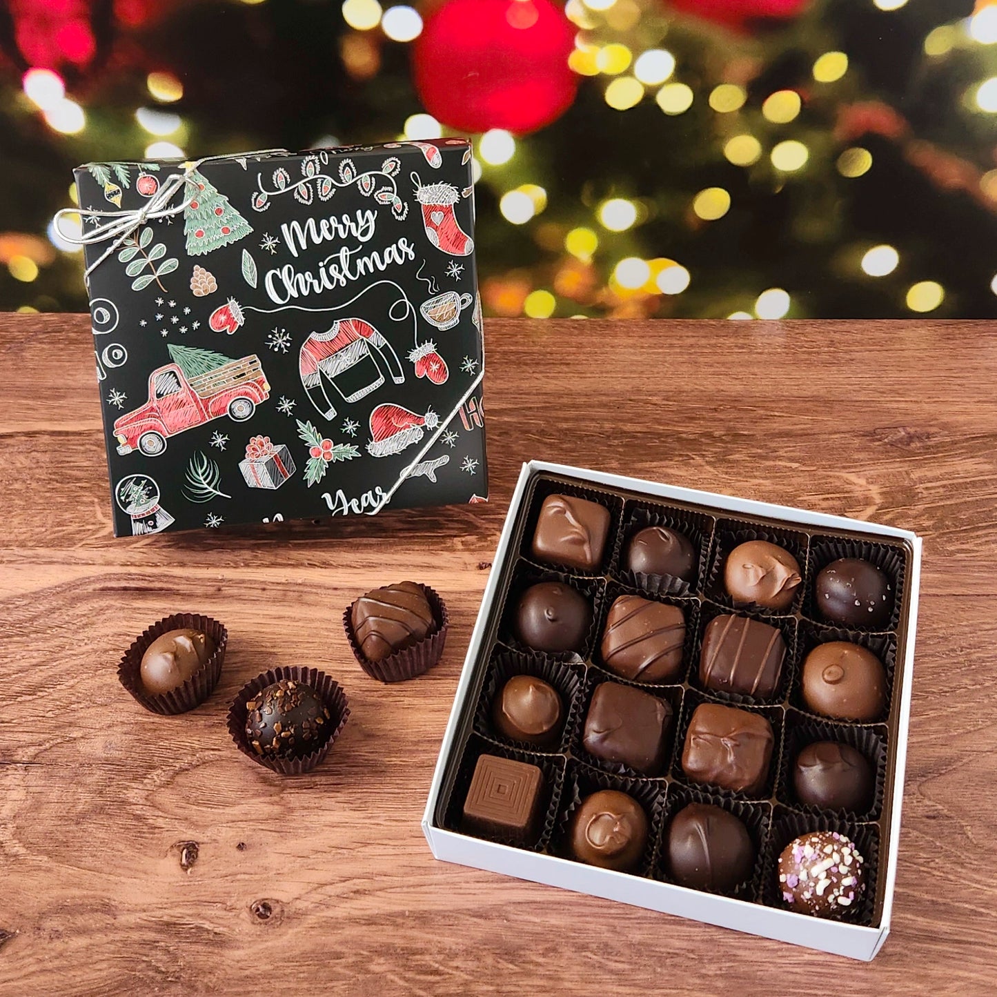 Box of chocolates with a Christmas-themed design on a wooden surface with blurred festive lights in the background.