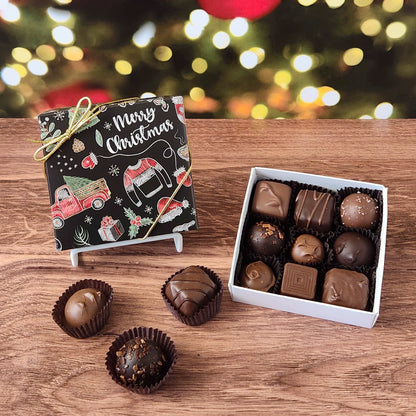 Box of chocolates with a 'Merry Christmas' design on a wooden surface with festive lights in the background.