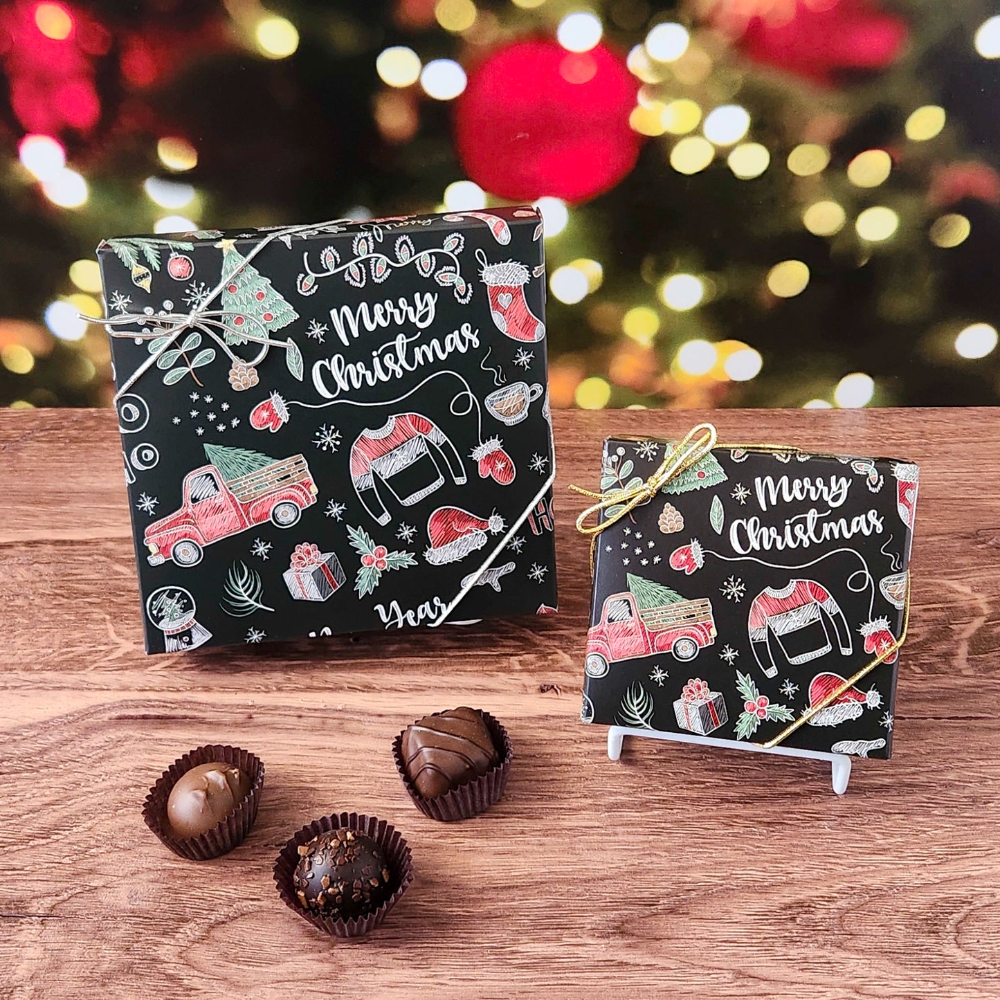 Two small Christmas-themed boxes with candy on a wooden surface, blurred festive lights in the background.