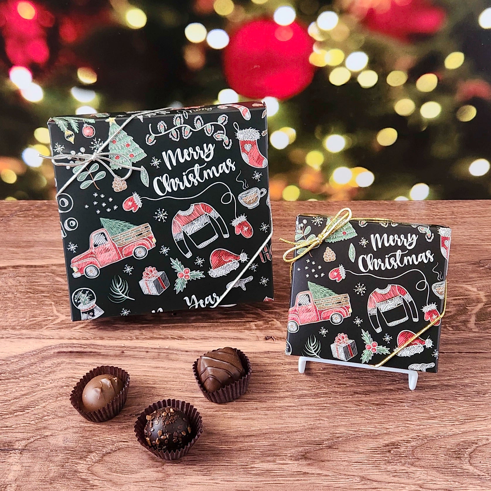Two small Christmas-themed boxes with candy on a wooden surface, blurred festive lights in the background.