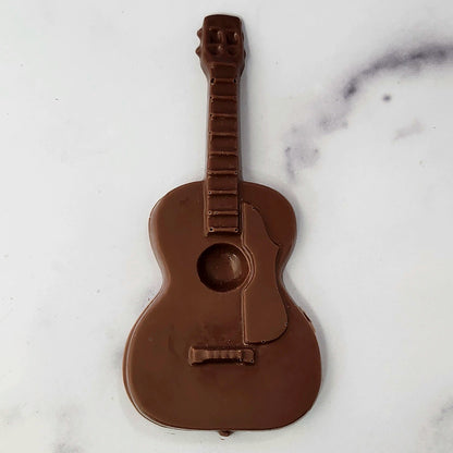 A chocolate guitar-shaped item on a white marble surface.