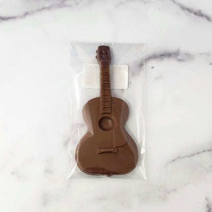 A chocolate guitar-shaped item sealed in a clear plastic bag, placed on a white marble surface.