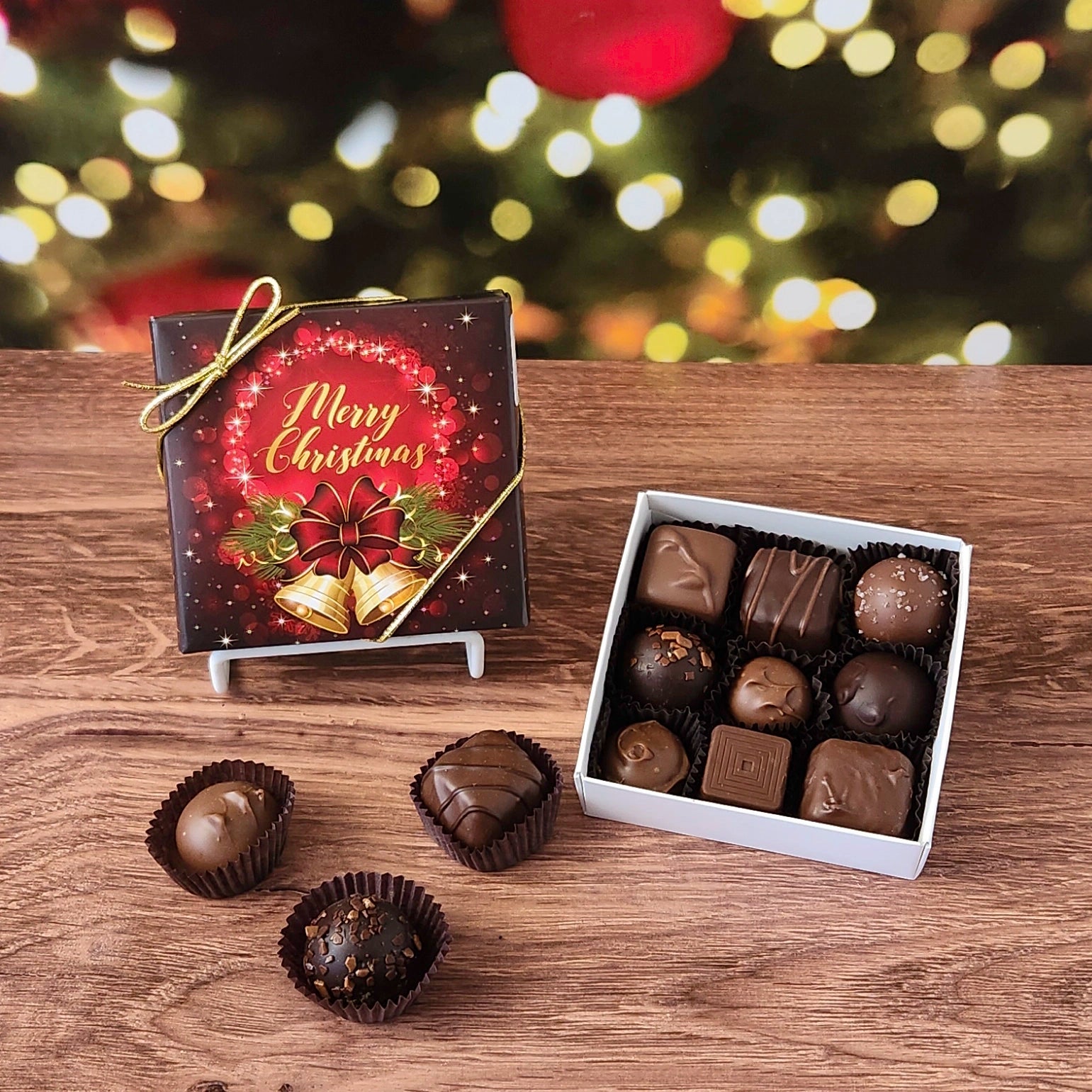 Box of chocolates with a 'Merry Christmas' box on a wooden surface with a festive background.