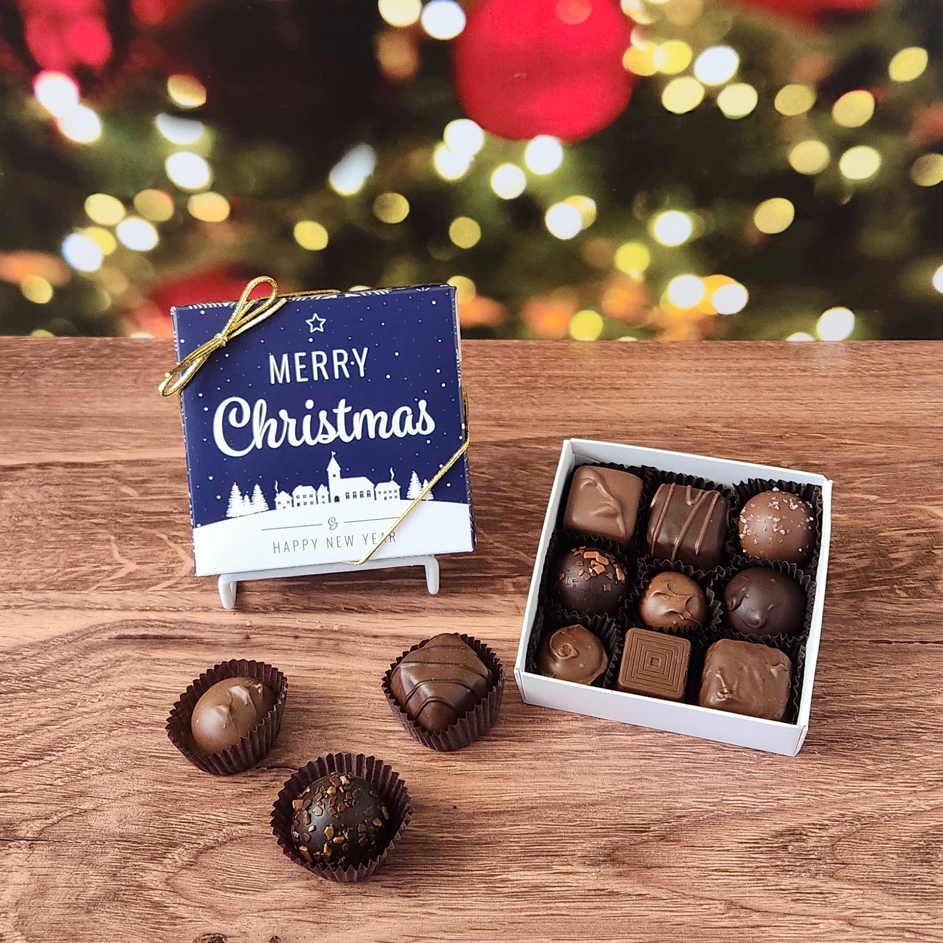 Box of chocolates with a 'Merry Christmas' box on a wooden surface with a festive background.