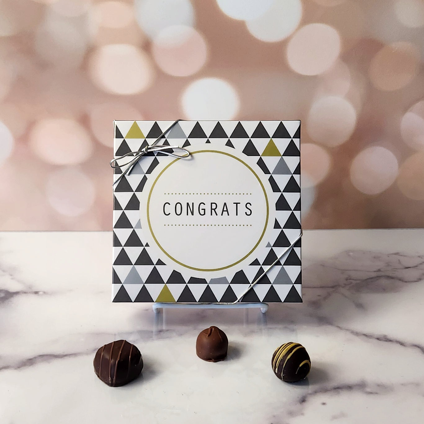 An assortment of our most popular milk and dark chocolate creams, caramels, melt-aways, and truffles all packed inside a festive box. On the cover of the box the word CONGRATS is printed surrounded by a grey and gold motif.