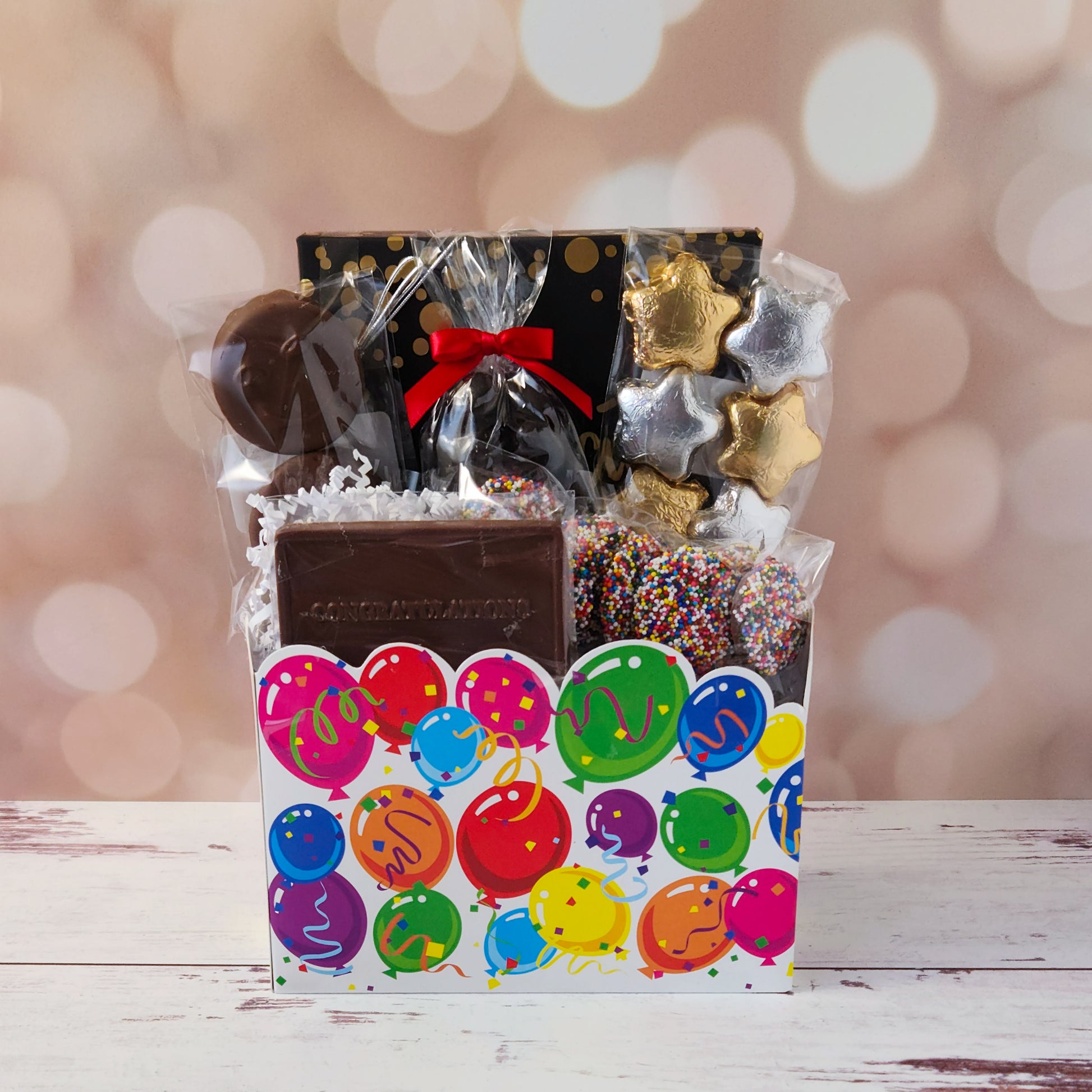 Make life’s big moments even sweeter with our Celebrate Gift Basket!
Inside, you’ll find a mix of gold and silver foiled milk chocolate stars, two chocolate-covered Oreo cookies, and classic milk chocolate nonpareils. A milk chocolate card that says “Congratulations”, dark chocolate-covered cranberries and a luxurious 16-piece assortment of creams, caramels, meltaways, and truffles. All overwrapped with a bow and ready for gifting!