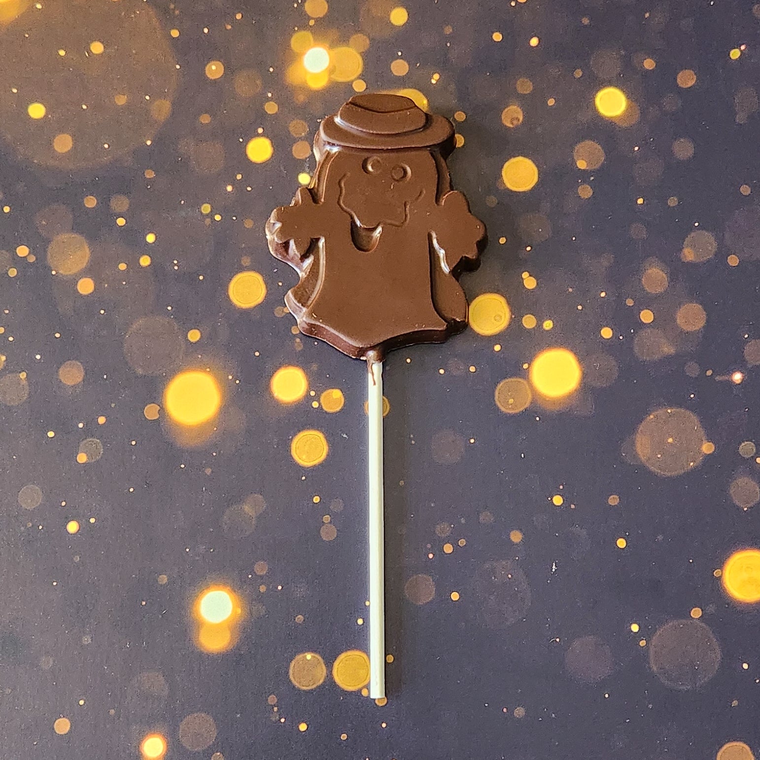 Dark Chocolate Ghost with hat Lollipop.  Measuring approximately 2.75 inches wide by 3.25 inches tall (excluding the pop stick) 