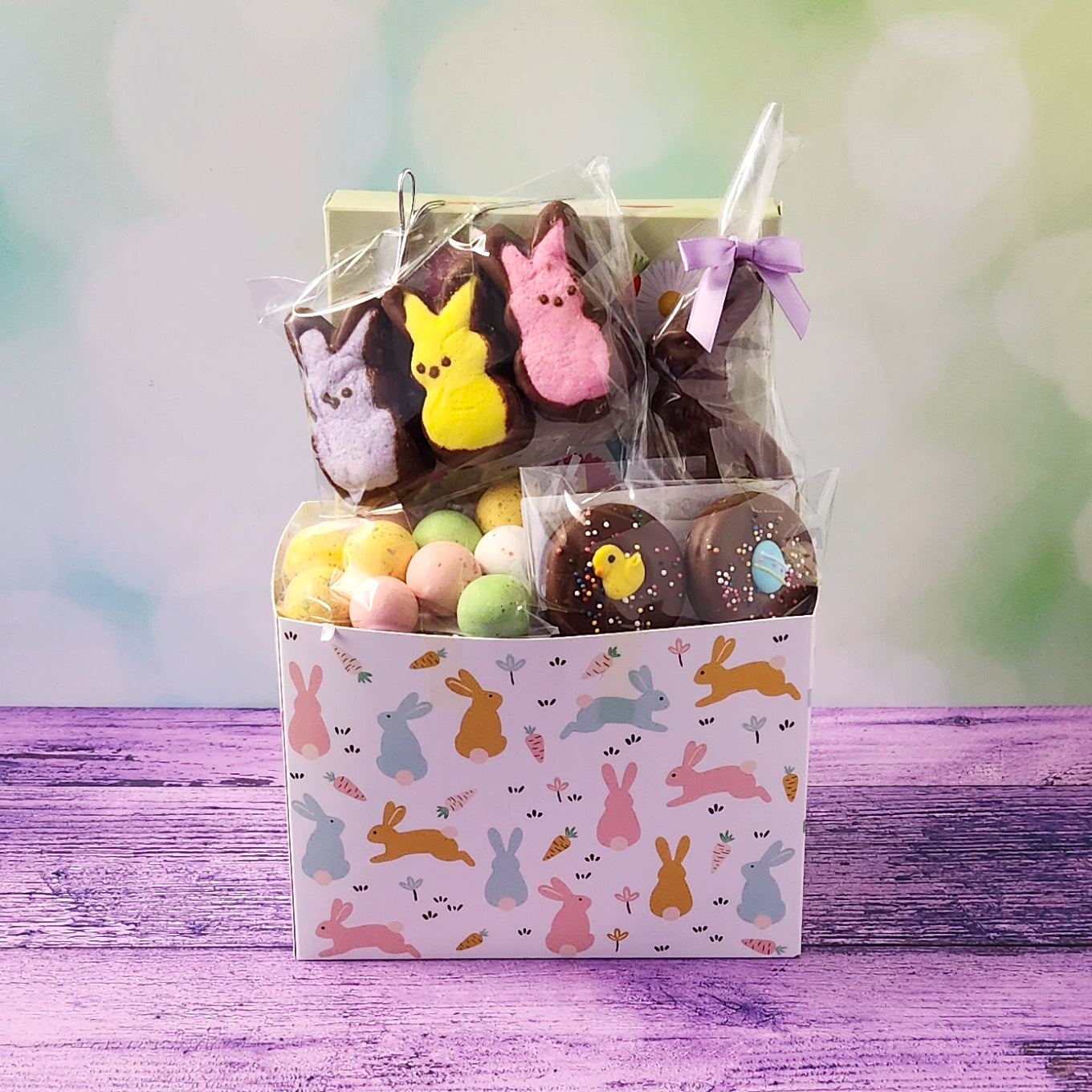 Easter-themed gift basket with pastel-colored treats and a decorative box on a wooden surface.