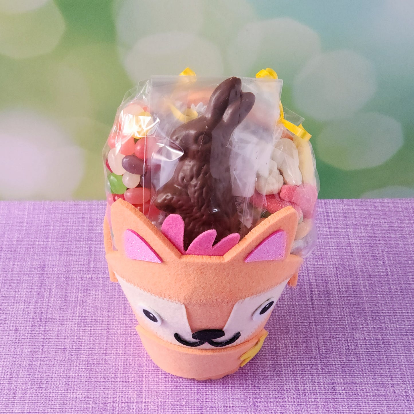 The basket base is an adorable felt fox, filled with an irresistible assortment of Chocolate-Dipped Marshmallow Peeps, fruity Jelly Beans, Sanded Gummi Bunnies, and a delicious Chocolate Bunny Favor. Finished with overwrap and a festive bow, this basket is ready to gift