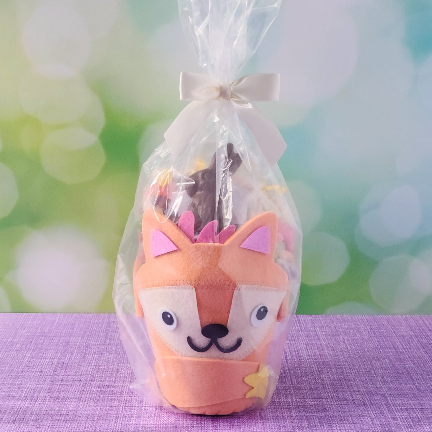 The basket base is an adorable felt fox, filled with an irresistible assortment of Chocolate-Dipped Marshmallow Peeps, fruity Jelly Beans, Sanded Gummi Bunnies, and a delicious Chocolate Bunny Favor. Finished with overwrap and a festive bow, this basket is ready to gift