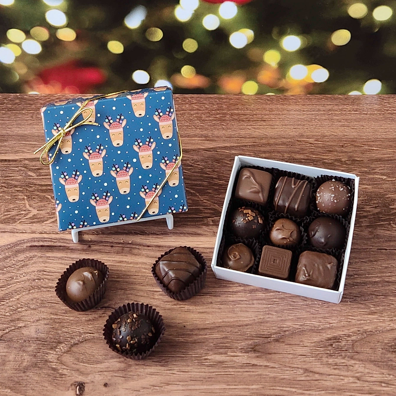9 piece box of chocolates with a blue reindeer-patterned box on a wooden surface with a blurred Christmas tree background.