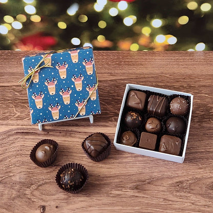 9 piece box of chocolates with a blue reindeer-patterned box on a wooden surface with a blurred Christmas tree background.