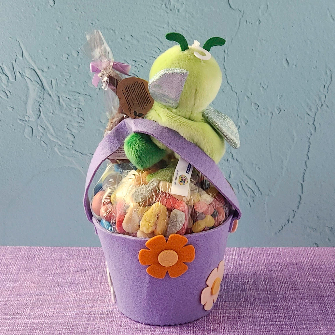 Purple gift basket with a plush toy and candies on a purple surface and gray background