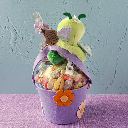 Purple gift basket with a plush toy and candies on a purple surface and gray background