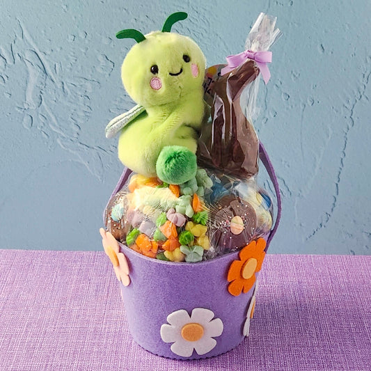 Purple bucket with a green plush toy and wrapped items on a purple surface.
