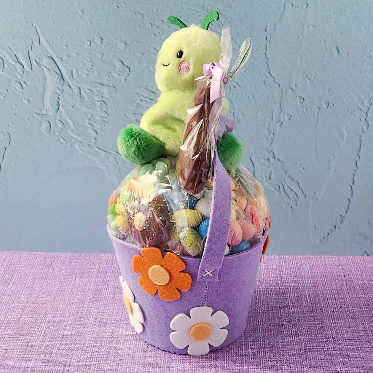 Purple gift basket with a plush toy and candies on a textured surface