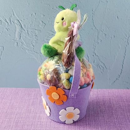 Purple gift basket with a plush toy and candies on a textured surface