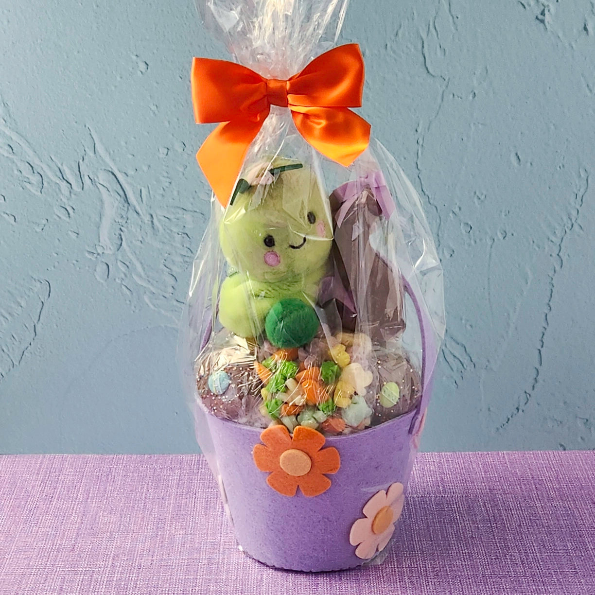 Gift basket with plush toy, candies, and a purple container on a gray background