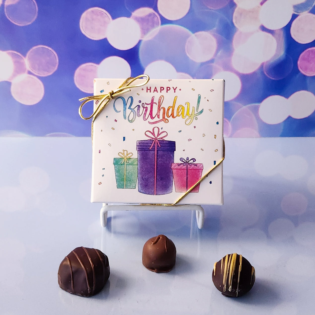 An assortment of our most popular milk and dark chocolate creams, caramels, melt-aways, and truffles all packed inside a festive box. The cover is printed with  the saying Happy Birthday sitting a top a pile of presents.