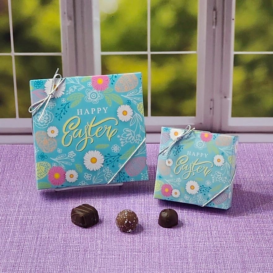 Two 'Happy Easter' boxes with decorative chocolates on a purple surface.