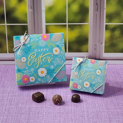 Two 'Happy Easter' boxes with decorative chocolates on a purple surface.