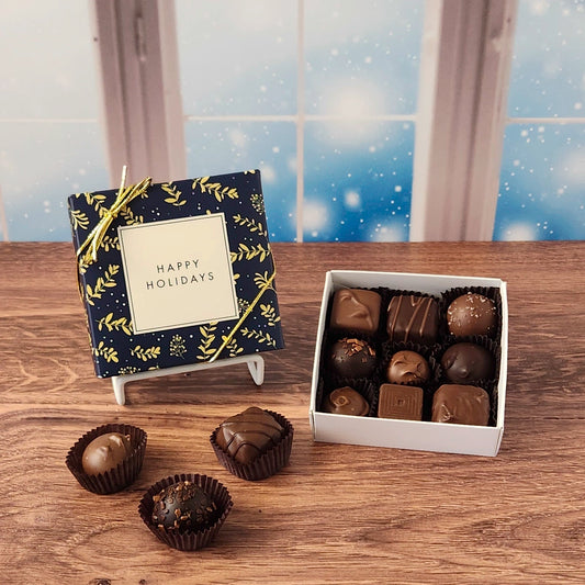 9 piece box of chocolates with  decorative Happy Holidays cover on a wooden surface and snowy background.