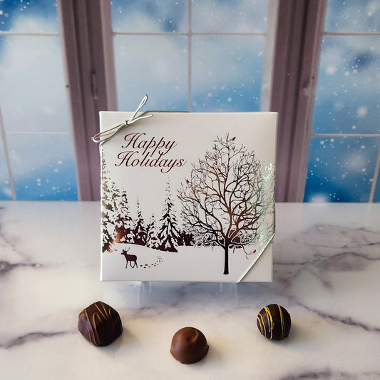 An assortment of our most popular milk and dark chocolate creams, caramels, melt-aways, and truffles all packed inside a box with the words "Happy Holidays" with a beautiful snow scene printed on the cover.