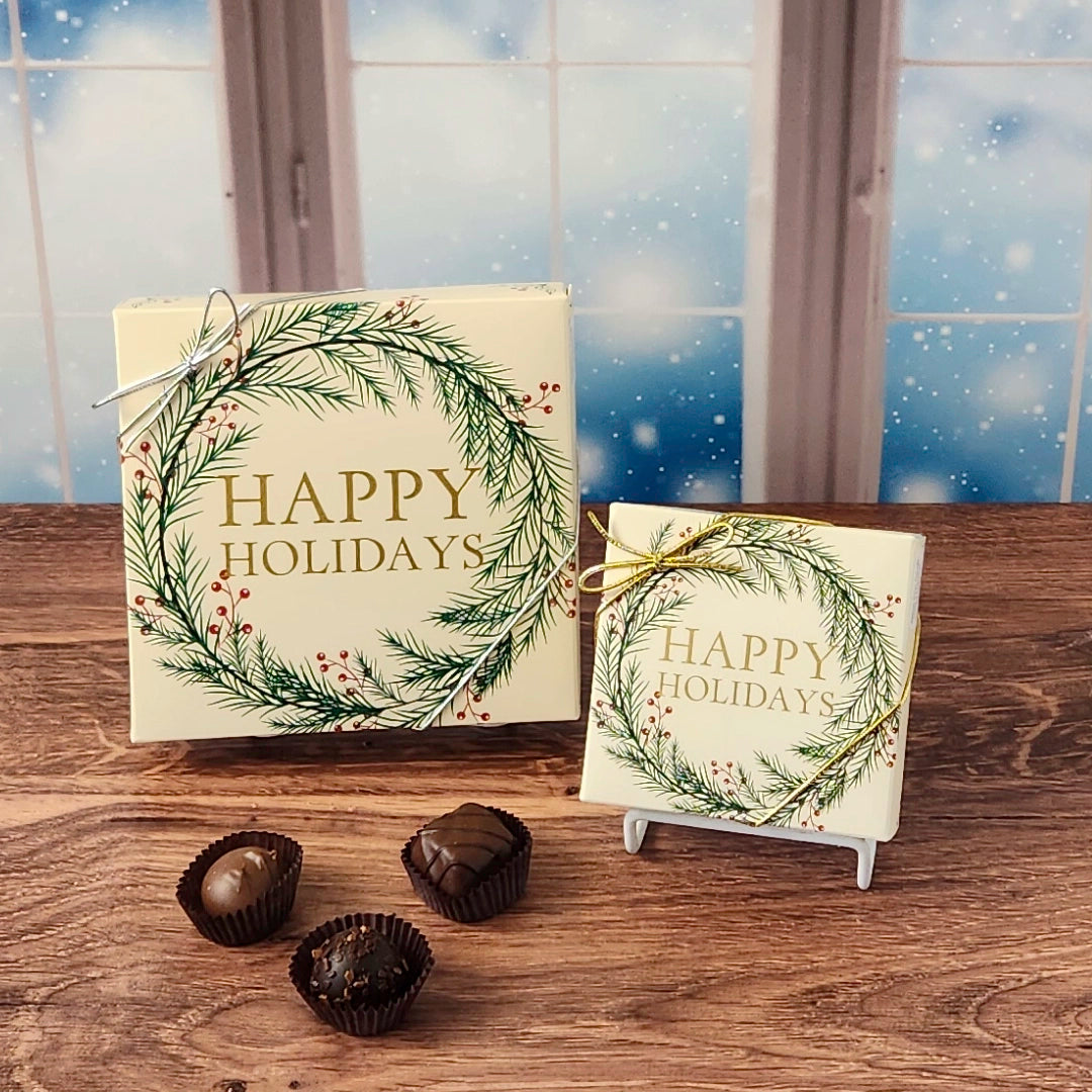 Box of chocolates with  decorative Happy Holidays wreath cover on a wooden surface and snowy background.  Available in 9 or 16 pieces