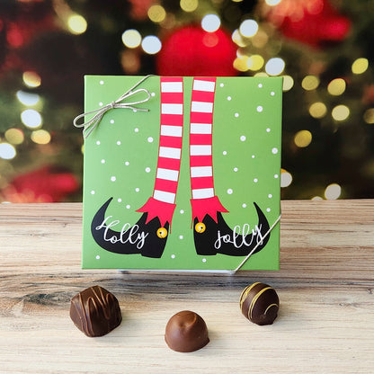 An assortment of our most popular milk and dark chocolate creams, caramels, melt-aways, and truffles all packed inside a box with the words "Holly Jolly" are written across a whimsical pair of Elf Feet printed on the cover.