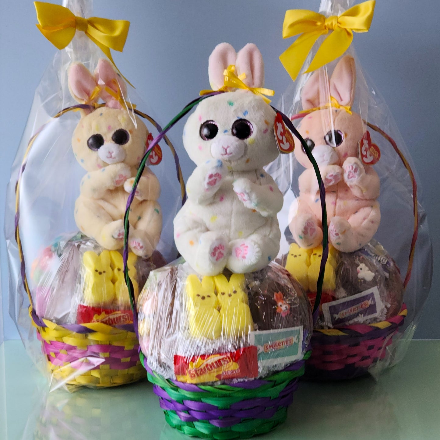 Each basket contains marshmallow peeps, gummy eggs and bunnies, a chocolate covered Easter Oreo, Easter Egg malt balls, jelly beans, a milk chocolate bunnies, lots of yummy kids candy and is topped off with a TY Stuffed Animal Easter Bunny. We finish the basket with overwrap and a bow so that it is ready to gift!

*** Due to the limited quantity of baskets we cannot guarantee specific colors. Photos are for example only and basket color may differ from the ones shown.