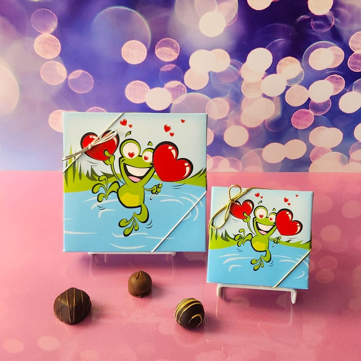 An assortment of our most popular milk and dark chocolate creams, caramels, melt-aways, and truffles all packed inside a festive box. On the cover of the box is a happy frog leaping while holding two hearts.