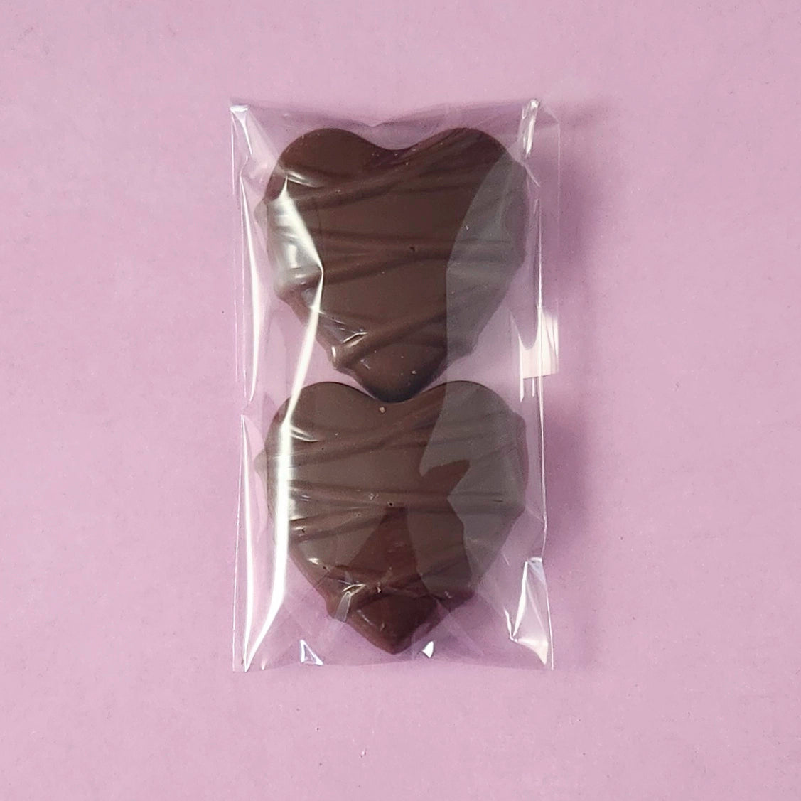 Two milk chocolate hearts in a clear plastic bag on a light purple background