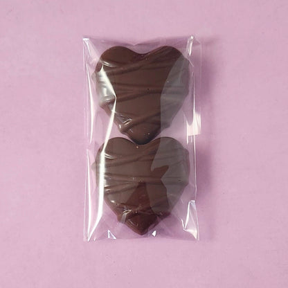 Two milk chocolate hearts in a clear plastic bag on a light purple background