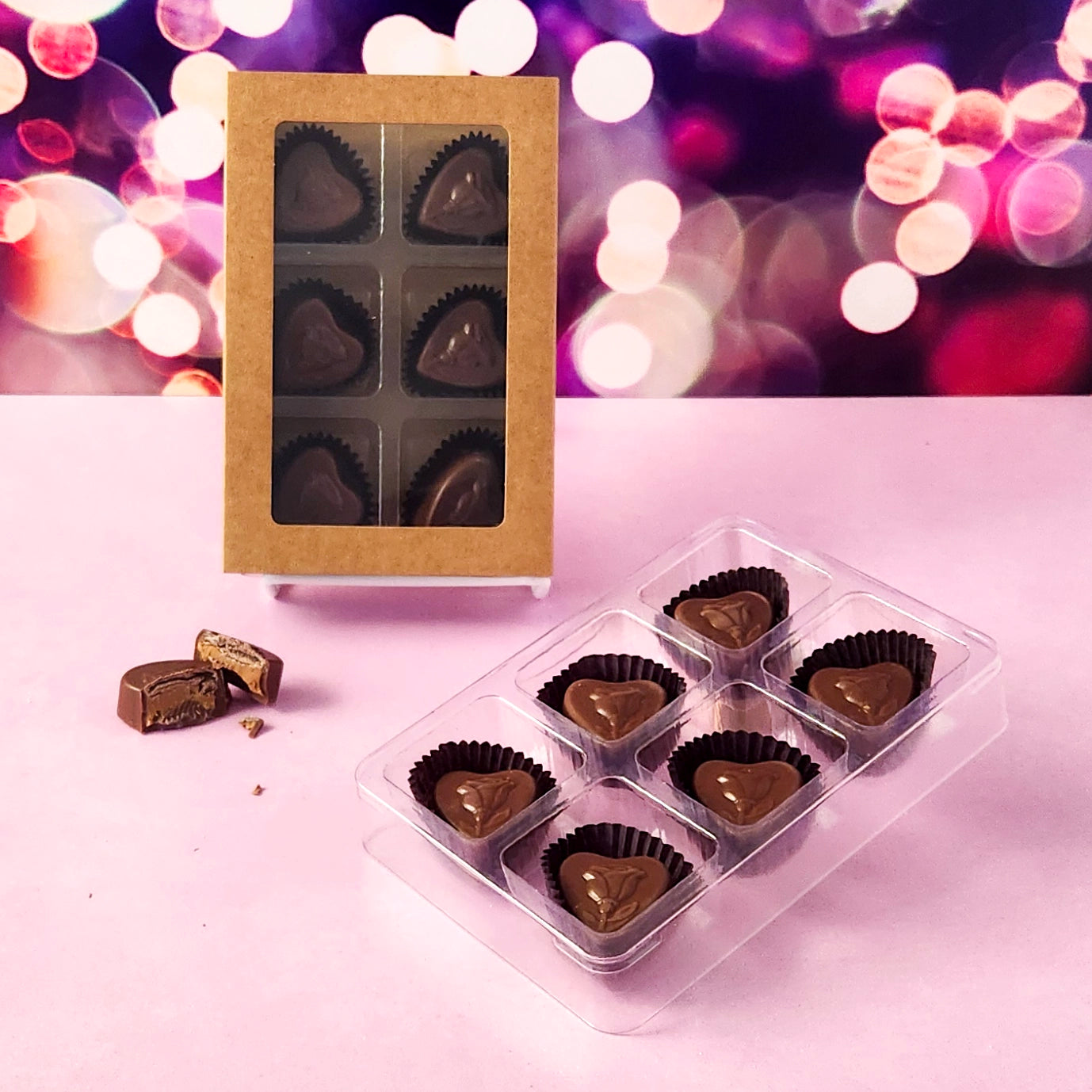 Heart-shaped chocolate candies in clear plastic packaging on a pink surface with a blurred valentines background.