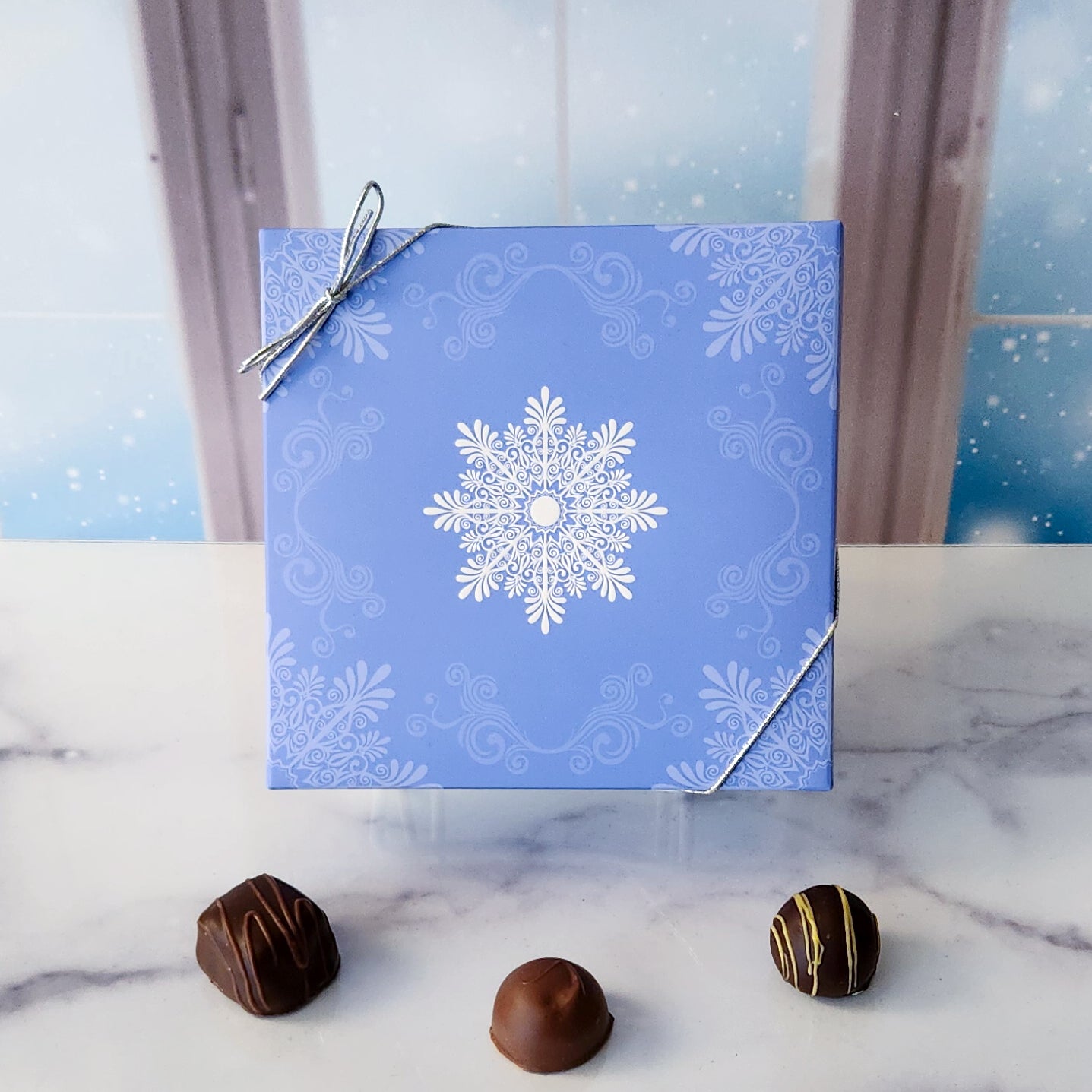 An assortment of our most popular milk and dark chocolate creams, caramels, melt-aways, and truffles all packed inside a box with an elegant snowflake printed on a pale blue cover.